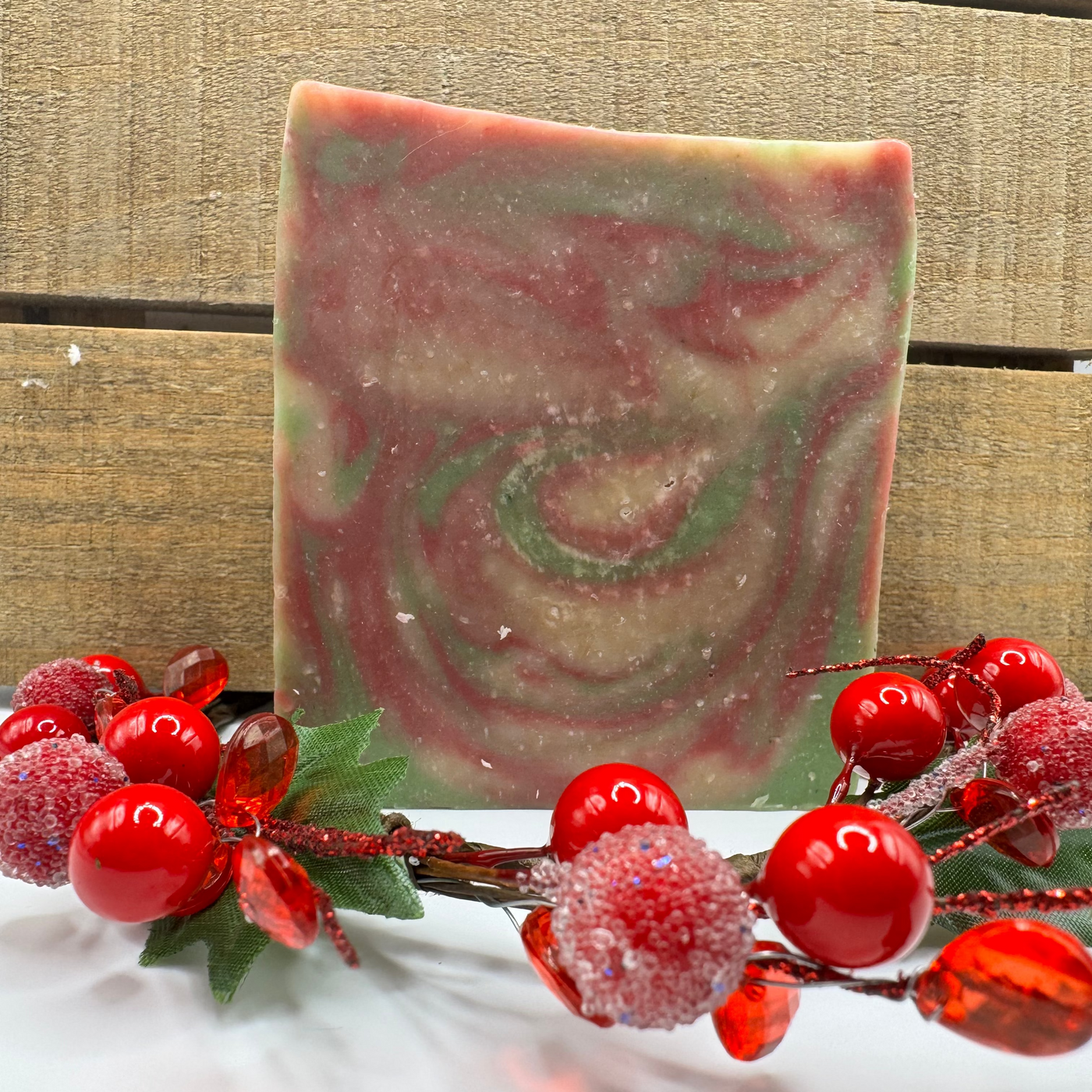 Marbled soap bar with red and green swirls on a wooden surface with decorative berries.