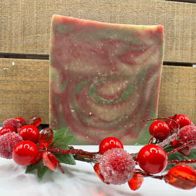 Marbled soap bar with red and green swirls on a wooden surface with decorative berries.