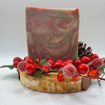 Handmade soap bar with red berries and a pine cone on a white background