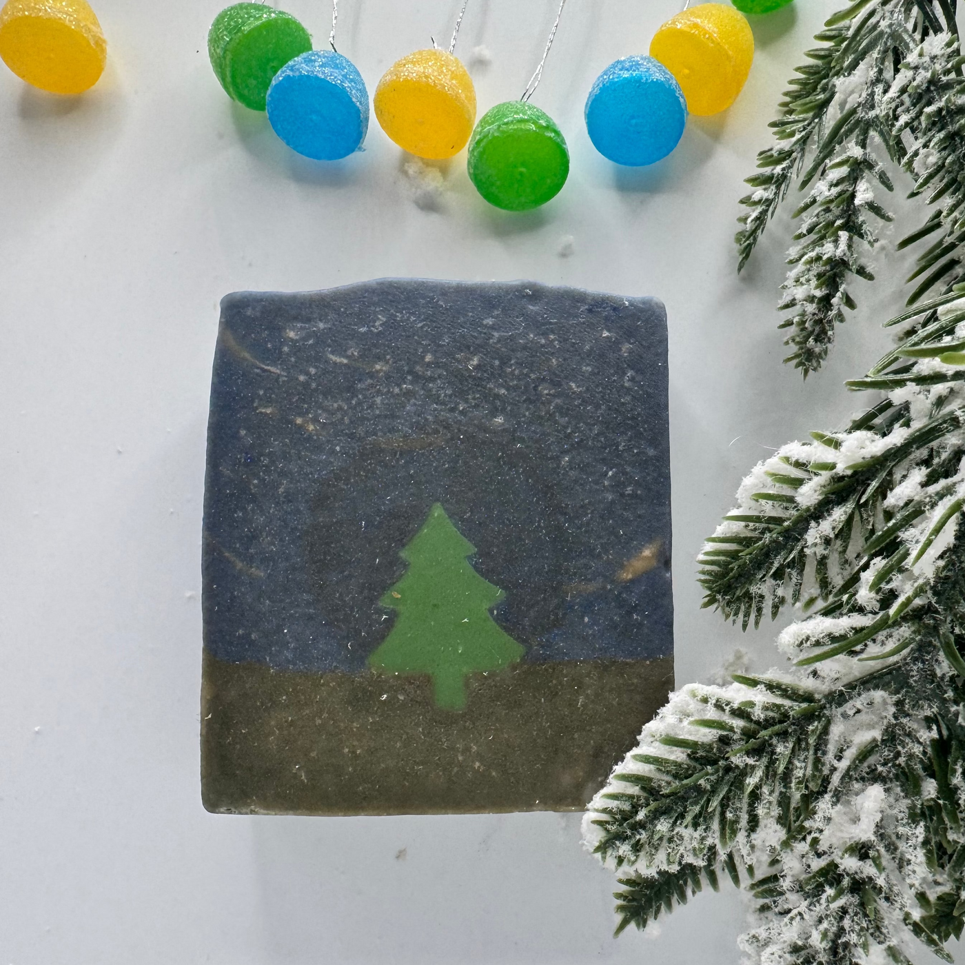 Decorative soap with a tree design on a white surface with colorful lights and snow-covered branches.
